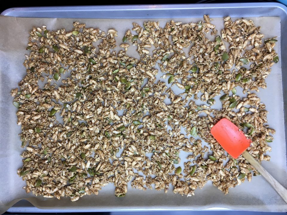 Granola is all mixed and spread out on parchment paper.